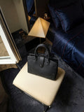 Clueless Paris black grained faux leather handbag with a structured design and top handle on a beige stool.