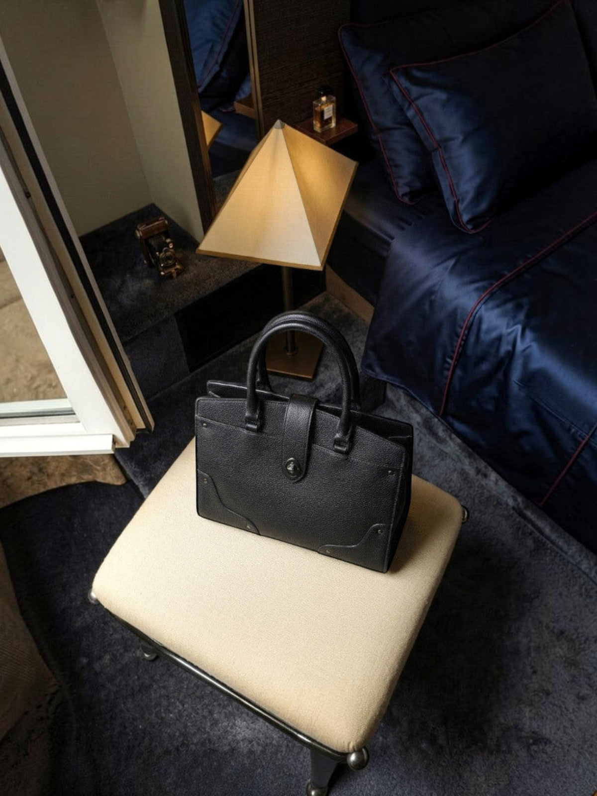 Clueless Paris black grained faux leather handbag with a structured design and top handle on a beige stool.