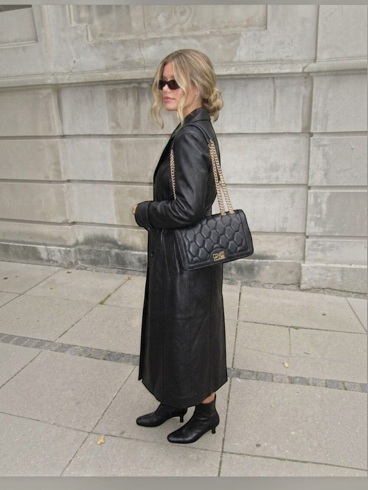 Clueless Paris black faux leather handbag with geometric quilting and gold chain strap worn by a woman in a coat