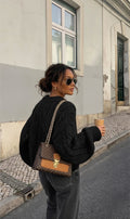 Femme portant un pull Clueless Paris noir en maille torsadée oversize avec un sac à main à bandoulière dans la rue