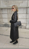 Sac à main noir Clueless Paris en polyuréthane avec logo métallique doré et bandoulière chaîne portée par une femme