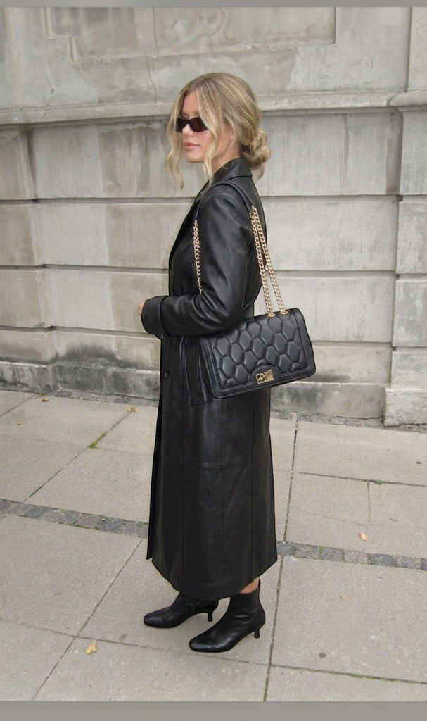 Sac à main noir Clueless Paris en polyuréthane avec logo métallique doré et bandoulière chaîne portée par une femme