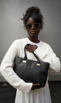 Femme portant un sac à main noir Clueless Paris en cuir grainé avec détails dorés et anses robustes