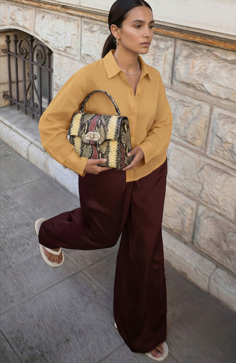 Femme portant un sac à main Clueless Paris structuré à motif serpent jaune, rouge et noir avec anse rigide.
