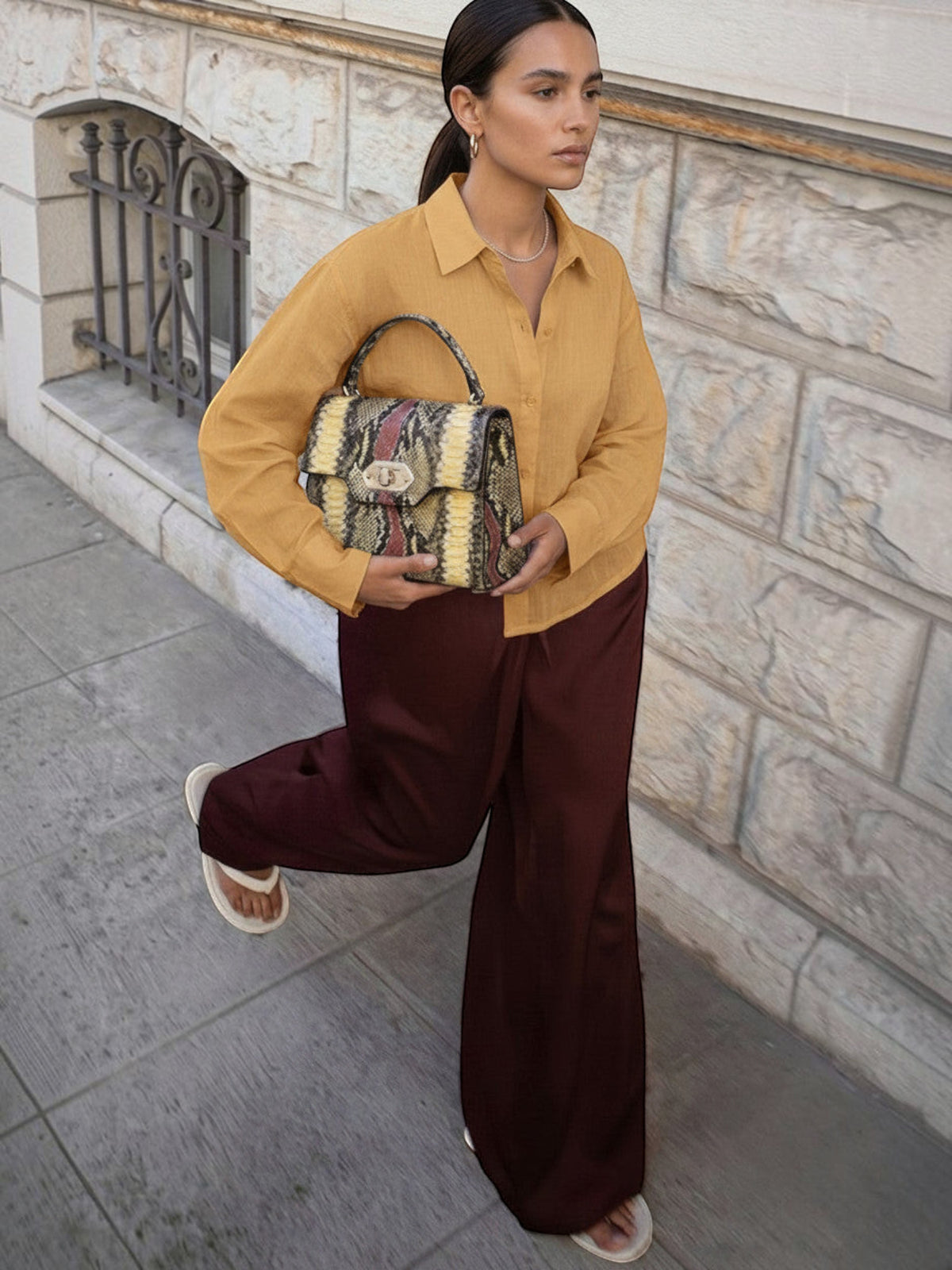 Clueless Paris elegant handbag with rigid handle and snakeskin pattern held by a woman in a mustard shirt