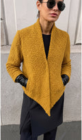 Veste courte texturée Clueless Paris couleur moutarde avec pan asymétrique et manches longues portées avec des gants